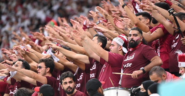 Eine Gruppe katarischer Fußballfans in roten T-Shirts, die koordiniert die Hände zum Jubeln heben