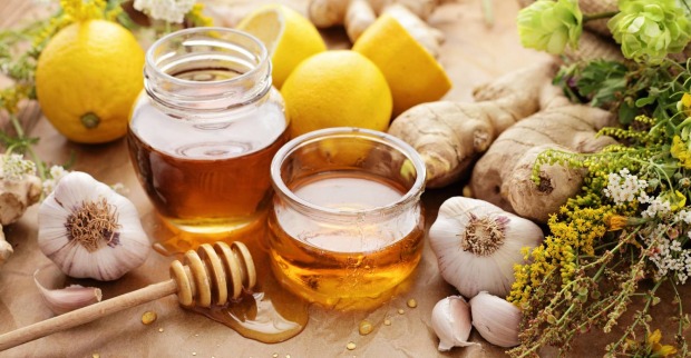 Zwei offene Gläser Honig, umgeben von Zitronen und Ingwer | Credit: iStock.com/KMNPhoto