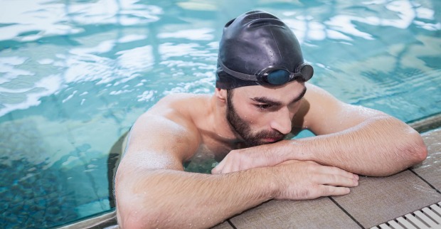 Mann mit Badehaube steht müde am Schwimmbeckenrand | Credit: iStock.com/Wavebreakmedia