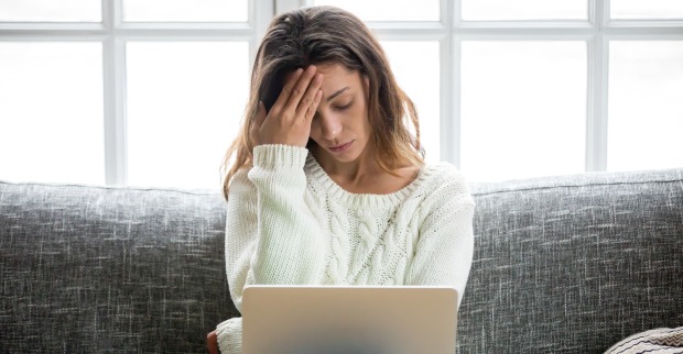 Eine Frau sitzt auf einem Sofa und beugt sich traurig über ihren Laptop.