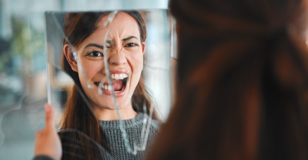 Junge Frau blickt in zerbrochenen Spiegel. | Credit: iStock.com/PeopleImages