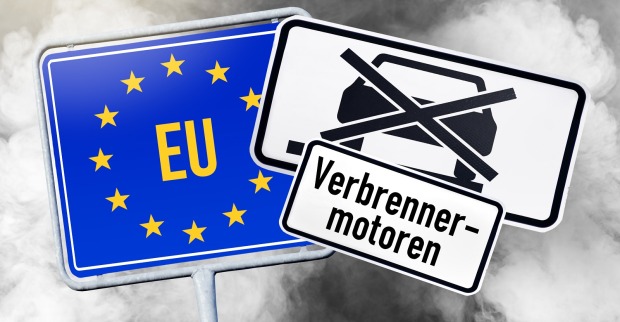 Ein EU-Ortsschild, ein Autoverbotsschild und die Aufschrift "Verbrenner-Motoren" vor dem Hintergrund von Autoabgasen