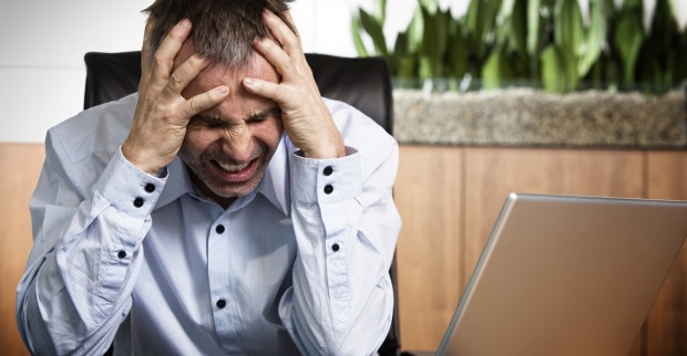 Mann mit Kopfschmerzen vor PC