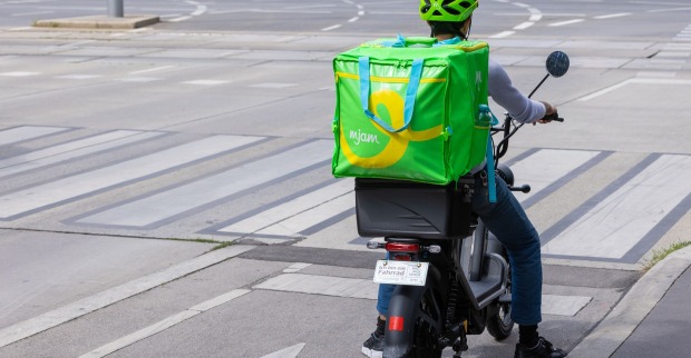 Ein mjam-Bote mit Lieferbox am Rücken an einer Straßenkreuzung.