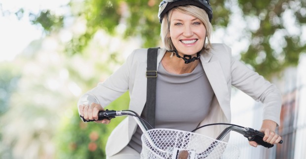 lächelnde Frau mit weißen Business-Outfit und Helm am Fahrrad | Credit: iStock.com/Wavebreakmedia