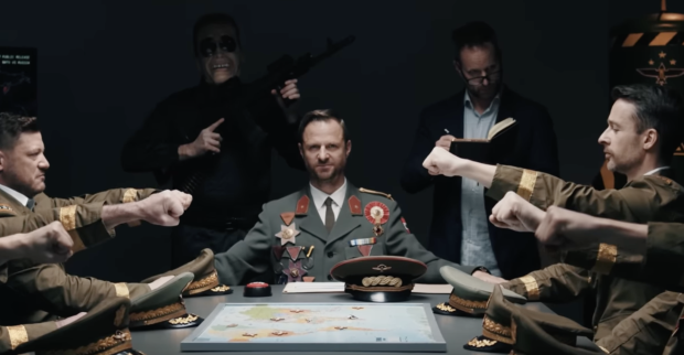 Hochmair in Uniform an einem Tisch mit Generälen. Hinter ihm schreibt Strolz in ein Buch