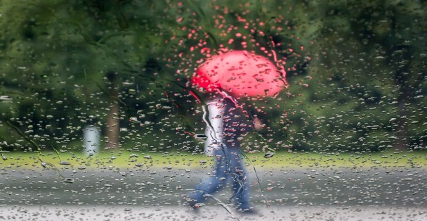 Jemand geht im Regen mit einem roten Schirm spazieren.