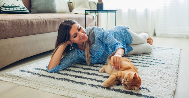 Junge Frau liegt mit ihrer Katze ausgestreckt auf dem Teppich | Credit: iStock.com/Maryviolet
