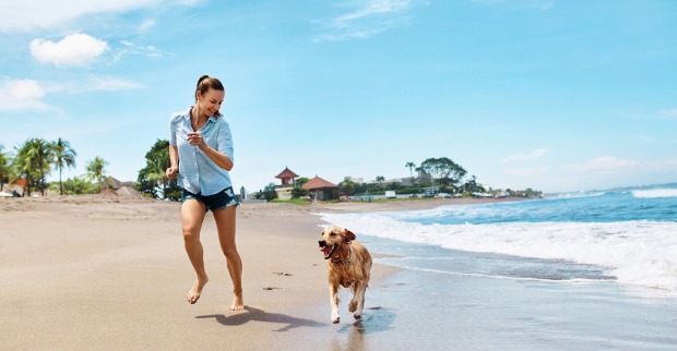 Frau rennt mit Hund am Strand entlang | Credit: iStock.com/puhhha