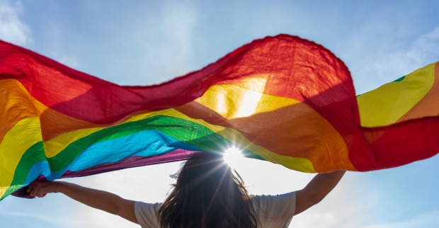 Frau hält Regenbogenflagge hoch in die Luft