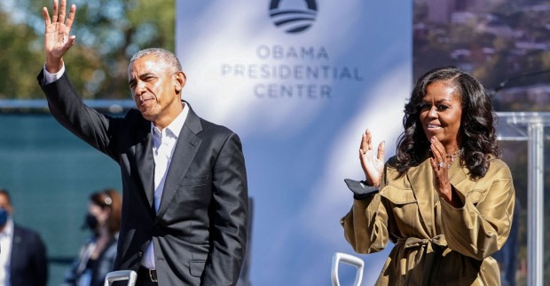 Barack und Michelle Obama klatschen und winken bei einer Veranstaltung.
