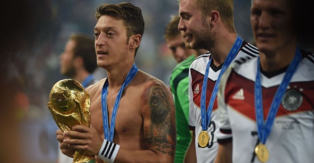 Mesut Özil hält die Weltmeisterkugel. Er hat kein Shirt an, auf seinem Arm ein großes Tattoo. Um den Hals die Medaille.