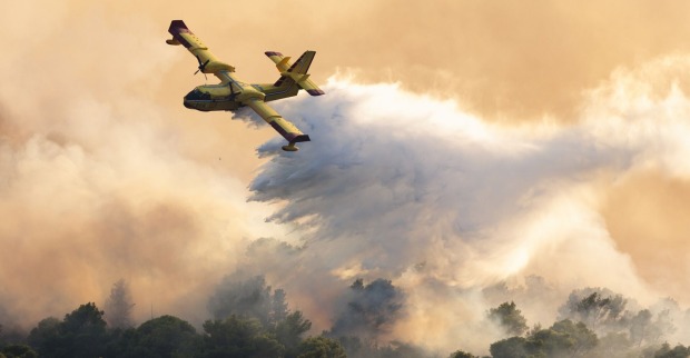 Ein Löschflugzeug leert seinen Wassertank über der brennenden Insel