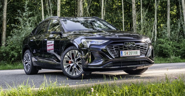 Der Audi Q8 e-tron Sportback frontal von vorne auf einer Straße, die durch einen Wald führt