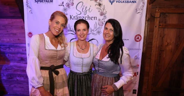 Drei Frauen im Dirndl vor einem Banner mit Sponsorenlogos und dem Schriftzug "Sisi Kränzchen"