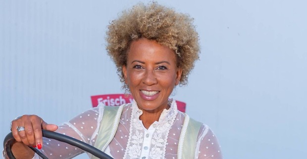 Arabella Kiesbauer in einem Dirndl mit blond gefärbten Haaren vor einer weißen Wand