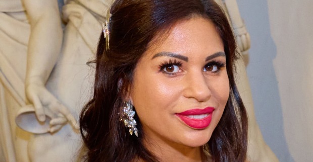 Nina Bambi Bruckner vor einer weißen Statue mit pinken Lippenstich und großen Ohrringen.