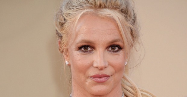 Britney Spears mit geschlossenen langen blonden Haaren vor einer Fotoleinwand