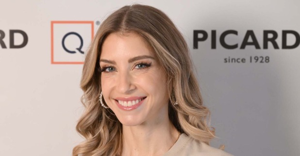 Cathy Hummels mit offenen blonden Haaren vor einer Fotoleinwand bei einem Event.