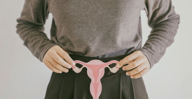 Frau hält Gebärmutter aus Papier vor Bauch