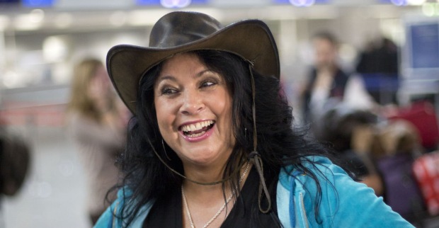Iris Klein mit einer blauen Weste und einem braunen Cowboyhut auf einem Flughafen.