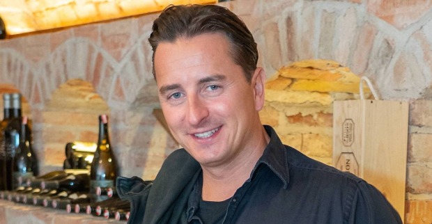 Andreas Gabalier steht in einem Weinkeller vor einem Weinregal.