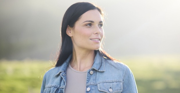 Anna Veith mit offenen schwarzen Haaren und einer blauen Jeansjacke vor einer grünen Wiese.