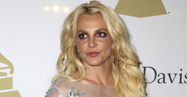Britney Spears vor einer Fotowand mit offenen blonden Haaren und einem silbernen Kleid.