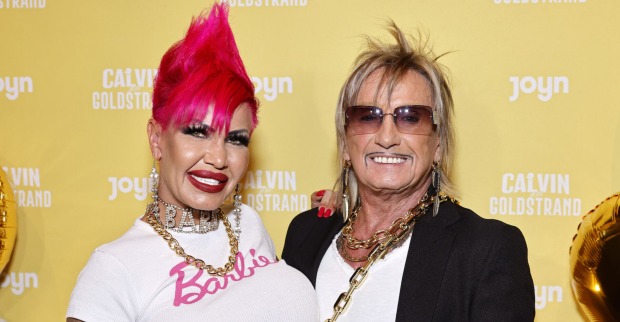 Gina trägt einen pinken Irokesen und ein weißes T-Shirt mit einer Aufschrift "Barbie". Bert Wollersheim hat blonde Haare und eine verdunkelte Sonnenbrille.