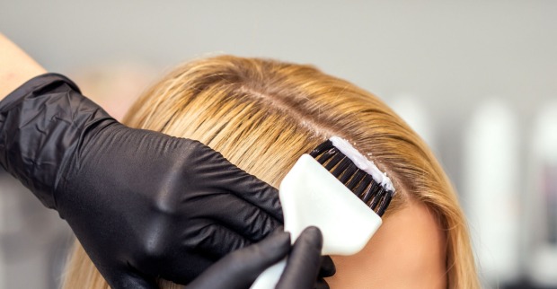 Der dunkle Ansatz eines blonden Haarschopfes wird nachgefärbt.