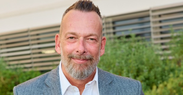 Robert Kratky aufgestellten Haaren in einem blauen Anzug vor einem Gebäude