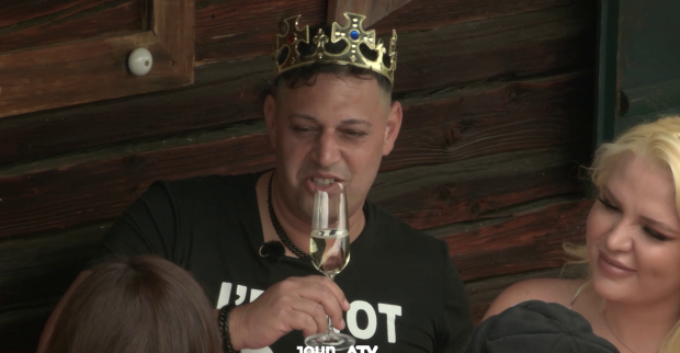 Forsthaus Rampensau Teilnehmer Marius mit einer Plastikkrone auf dem Kopf und einem Sektglas in der Hand.