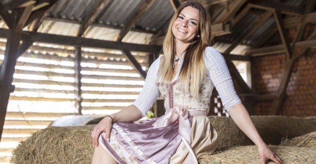 Kandidatin Nicole von Bauer sucht Frau posiert auf Strohballen mit einem rosa Dirndl und offenen blonden Haaren.