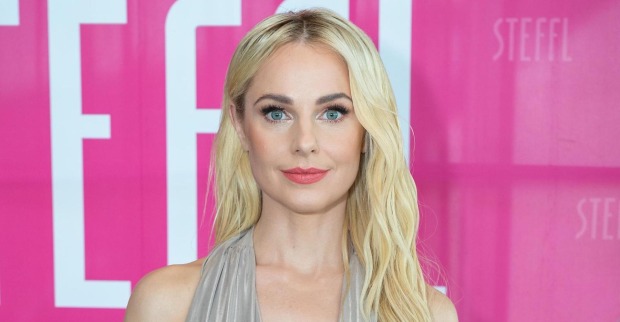 Silvia Schneider mit offenen blonden Haaren vor einer pinken Fotowand.
