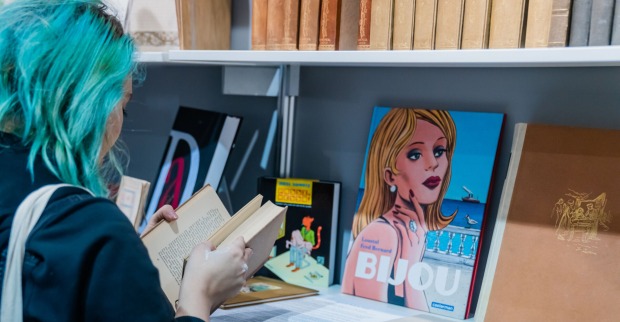 Junge Frau mit blauen Haaren in einem Buch blätternd, von hinten