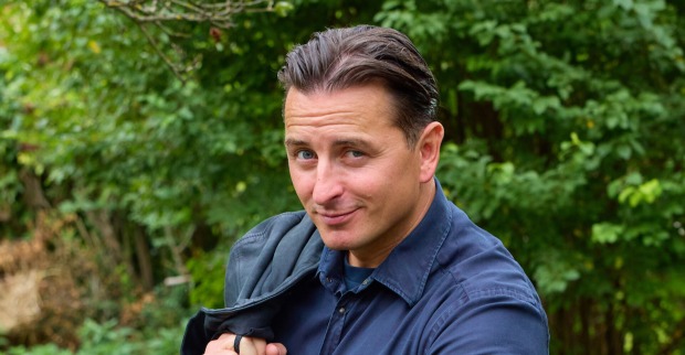 Andreas Gabalier steht vor einem grünen Busch. Er trägt ein dunkelblauen Hemd.