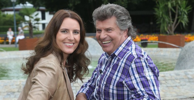 Andy Borg und seine Birgit posen vor einer Wiese auf einer Parkbank. Beide lächeln glücklich in die Kamera.