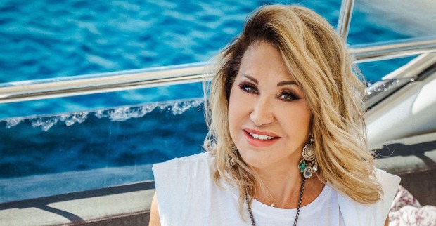 Carmen Geiss hat gewelltes blondes Haar und sitzt auf einer Yacht. Dahinter ist das blaue Meer.