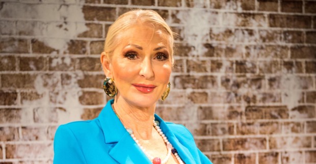 Désirée Nick trägt einen blauen Blazer, zurück gebundene Haare und steht vor einer braunen Ziegelwand.