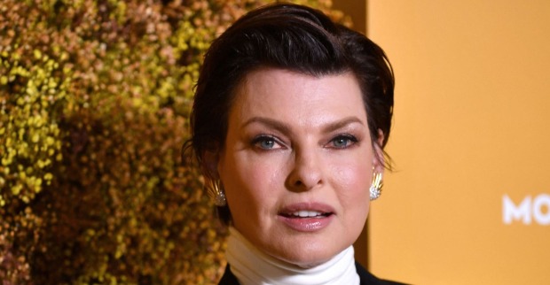 Linda Evangelista trägt einen weißen Rollkragenpullover und kurze zurück gegelte braune Haare.