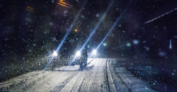 Ein Auto fährt nachts auf einer Schneefahrbahn.
