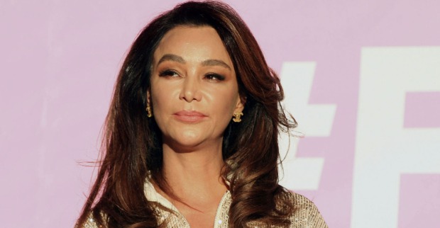 Verona Pooth trägt offene dunkle Haare und sitzt vor einer pinken Leinwand.