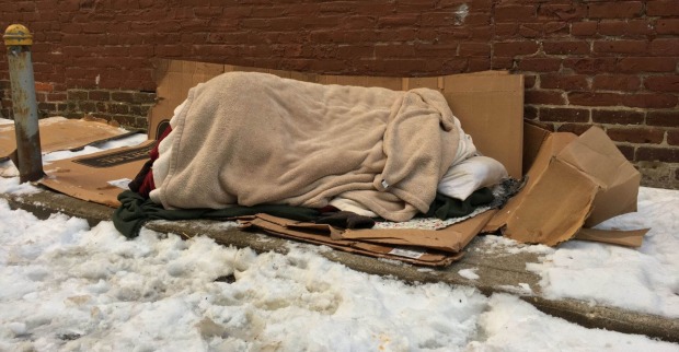 Ein Obdachloser schläft bei Schnee auf der Straße.