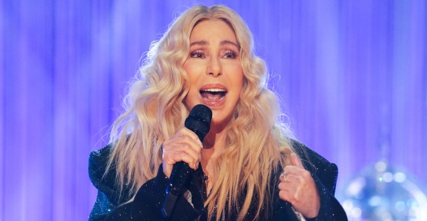 Cher mit blonden, gewellten Haaren und einem schwarzen Sakko. Sie singt in ein Mikrofon.