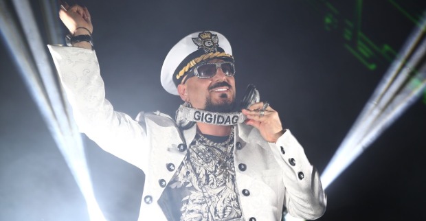 Gigi D'Agostino mit einer weißen Jacke und einem Kapitän-Hut bei einem DJ-Set.