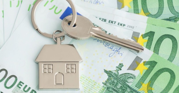 Ein Schlüssel mit einem Schlüsselanhänger in Form eines Haus liegt auf mehrern Hunderteuroscheinen