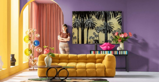 Wohnzimmer mit senffarbener Couch, lila wand, Frau im Hintergrund