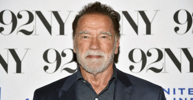 Arnold Schwarzenegger mit einem dunkelgrauen Smoking vor einer Fotowand.