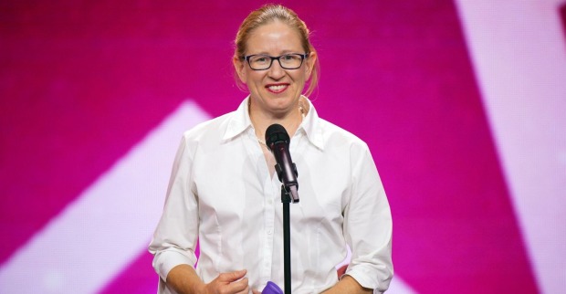Die australische "Das Supertalent" Teilnehmerin Beatrice McQueef steht vor einem Mikrofon und trägt ein weißes Hemd. Hinter ihr ist eine pinke Fotowand.