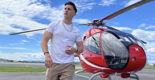 Satans Bratan mit einem weißen T-Shirt vor einem roten Helikopter.